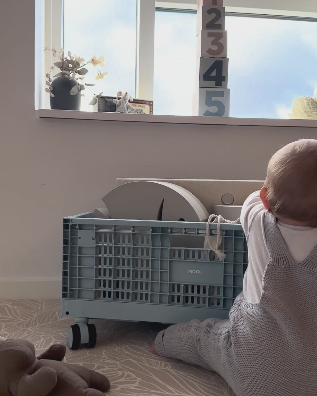 Video laden: Ein süßer kleiner Junge sitzt auf dem Boden und findet sein Lieblingsspielzeug in einer Modu-Aufbewahrungsbox und in einem Rice-Korb.